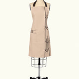 A beige apron with black geometric patterns and adjustable straps displayed on a mannequin.