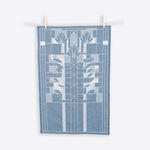 A blue and white cotton tea towel with a geometric waterlilies pattern hanging on two wooden clothespins against a white background.