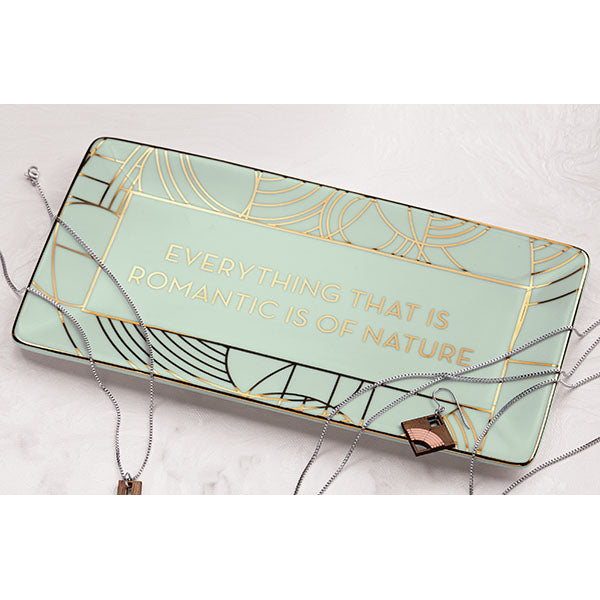 A rectangular porcelain tray with a geometric pattern, trimmed in gold, with the text 'EVERYTHING THAT IS ROMANTIC IS OF NATURE' across the center.