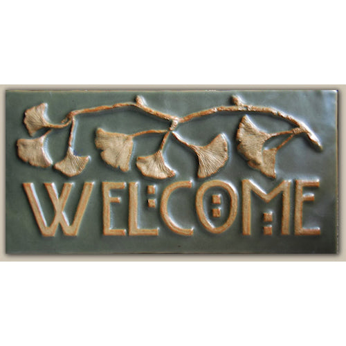 A hand pressed ceramic black tile with a relief design of Ginkgo leaves forming the word 'WELCOME'.