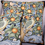Two square-shaped throw pillows with a floral and bird design, in green, blue, and brown colors, on a sofa.