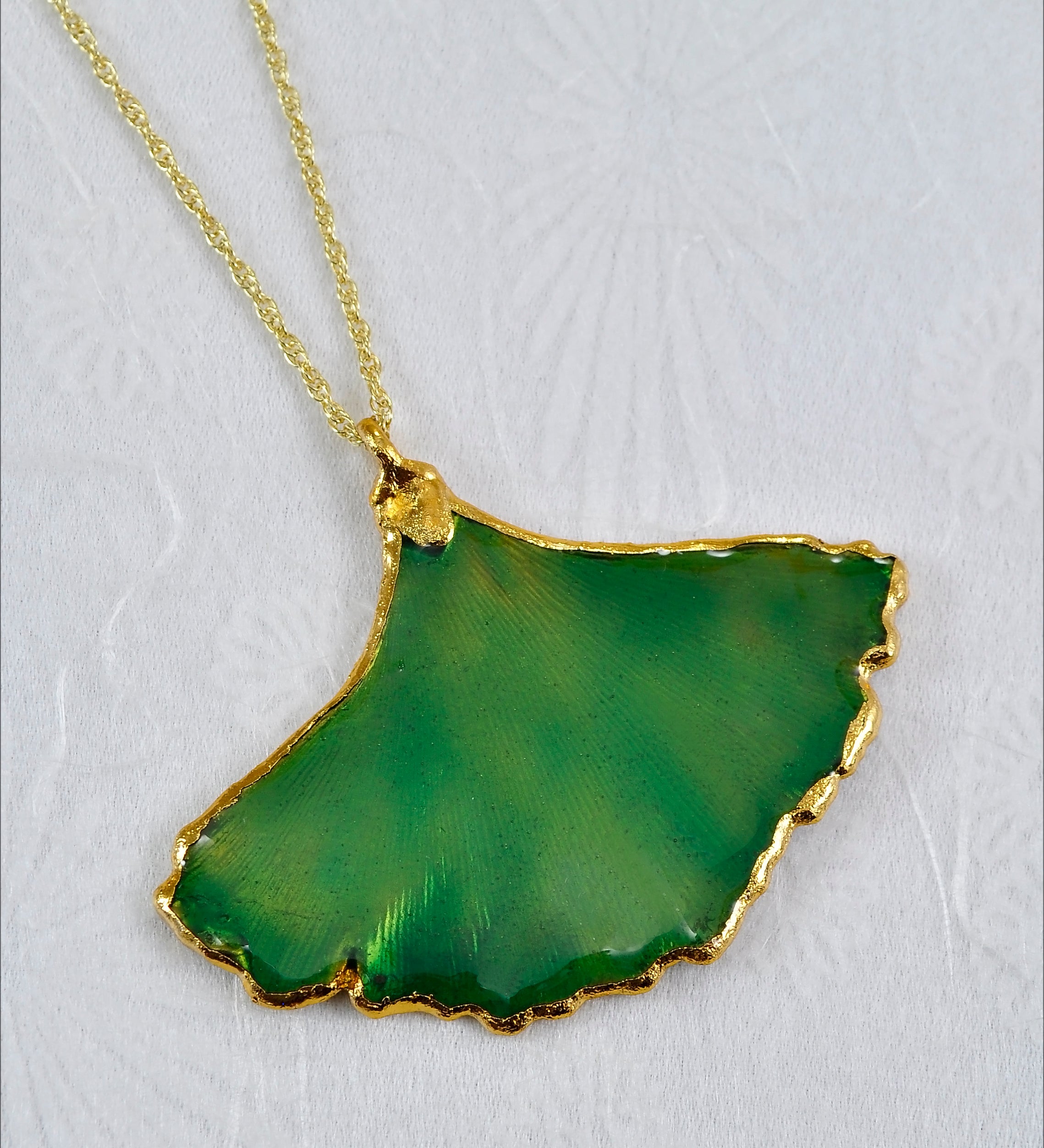 A necklace featuring a real Ginkgo Leaf shaped pendulum with a gold and lacquered green finish, attached to an 18-inch gold chain.