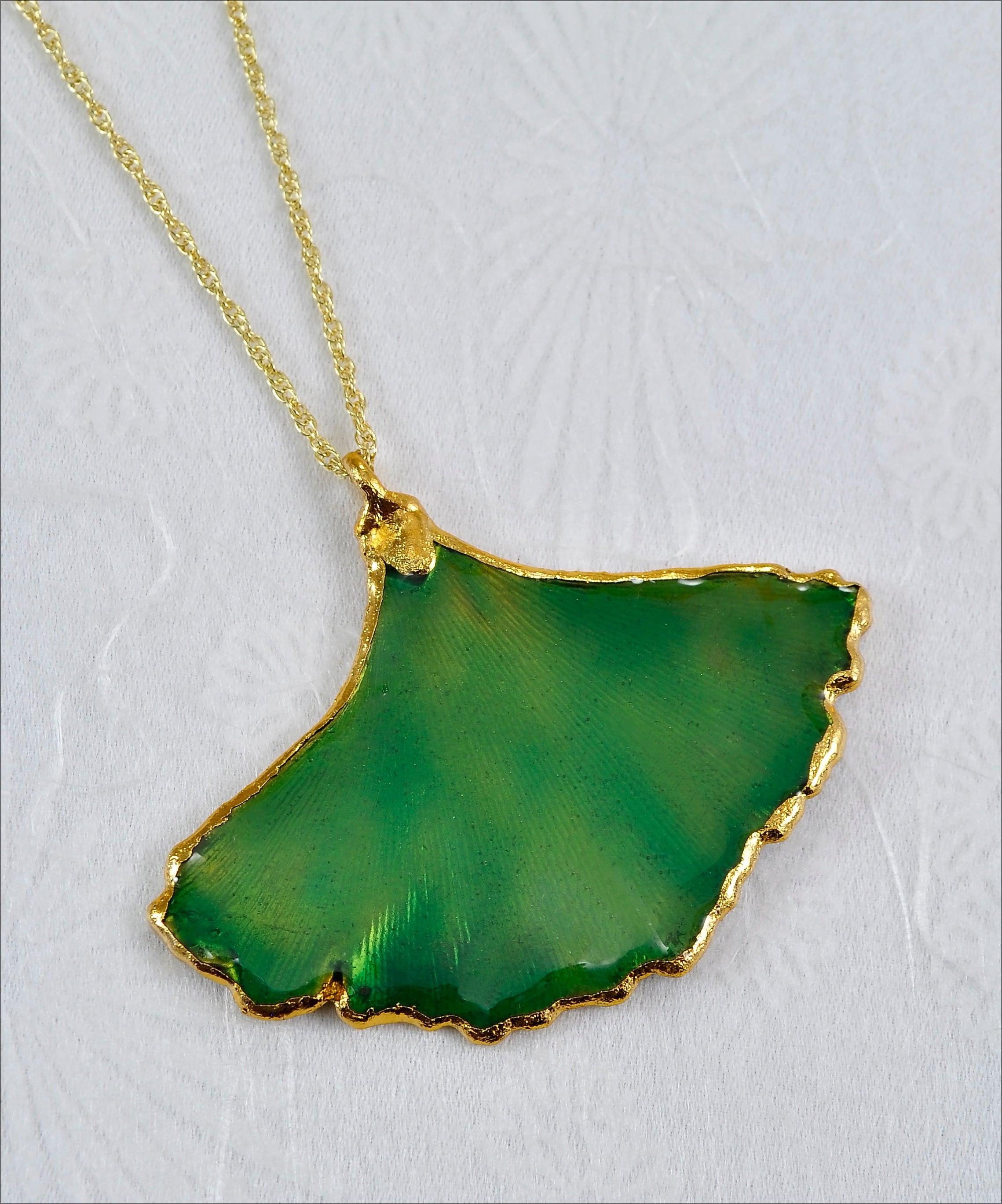 A necklace featuring a real Ginkgo Leaf shaped pendulum with a gold and lacquered green finish, attached to an 18-inch gold chain.
